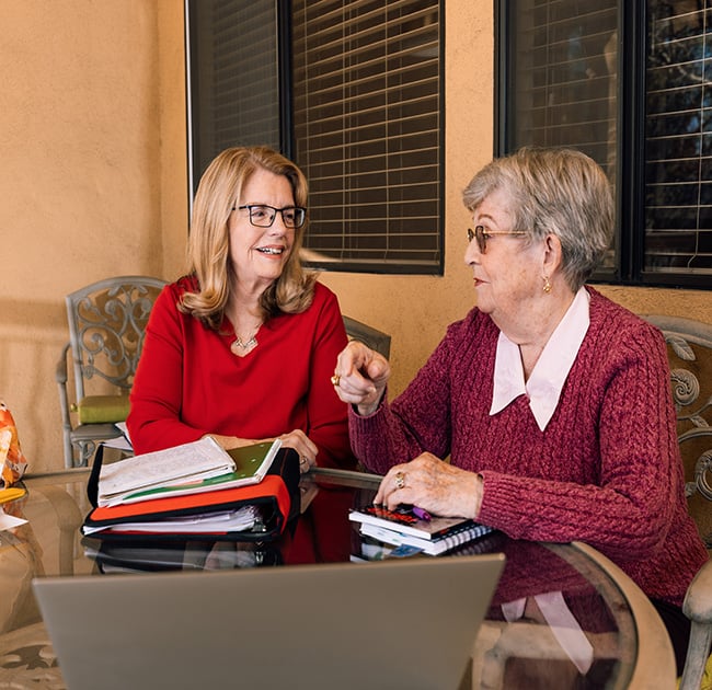 Two senior women with notebooks sit around a table during a writing group meeting at Plymouth Village