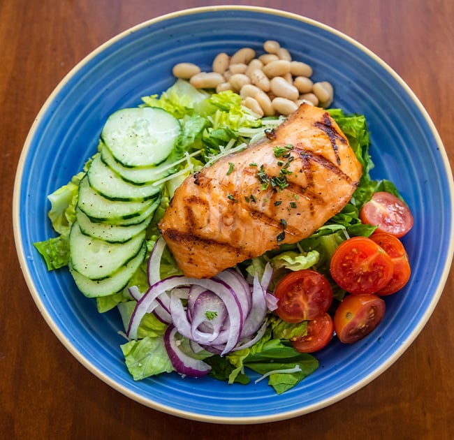 Salmon filet on a bed of lettuce, cucumber, onion, tomato and beans