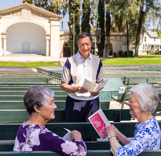 Two senior women and a senior man at an outdoor amphitheater holding programs from an event