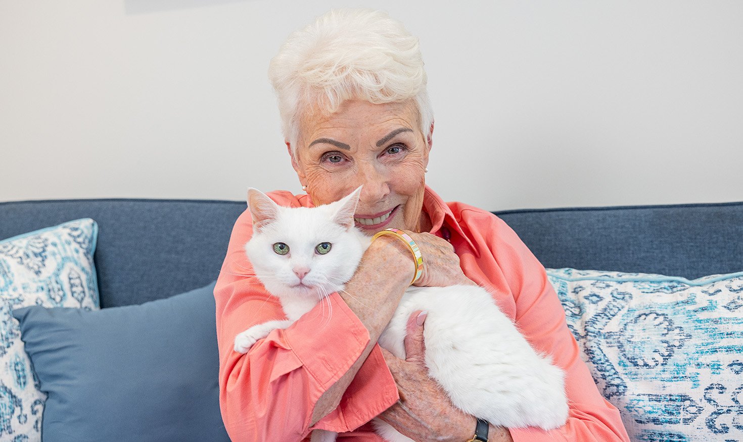 Smiling senior woman sitting on her couch and holding her white cat close 