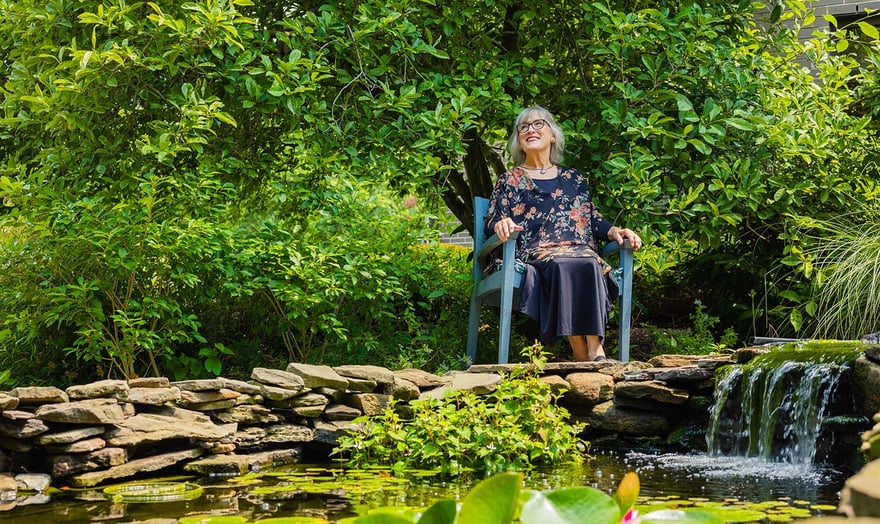 Senior woman sitting in a chair next to pond with a small waterfall