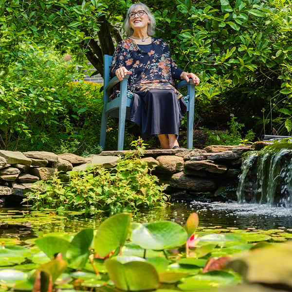 Senior woman sitting in a chair next to pond with a small waterfall