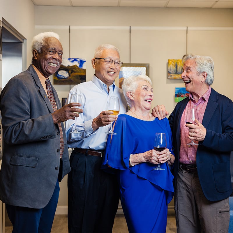 Three senior men and a senior woman in evening wear holding glasses of wine