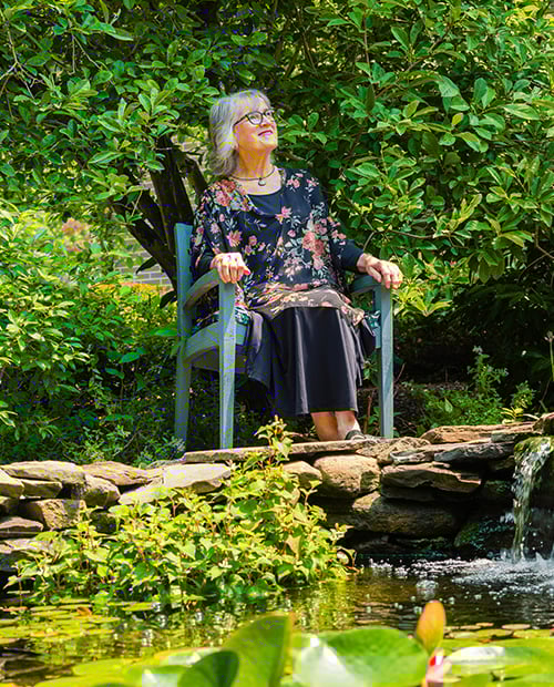 Senior woman sitting in a chair next to pond with a small waterfall