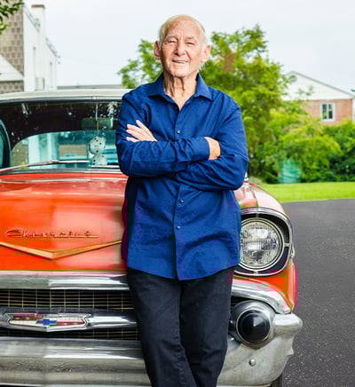 senior leaning on the hood of a red vintage car