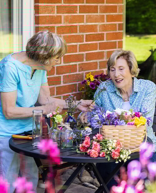 Two senior women at a patio table arranging flowers