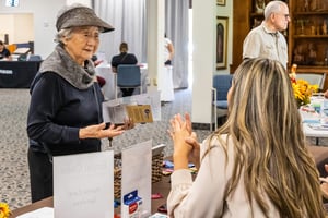 Senior woman holding brochures and talking to a woman at a table during an expo at Westminster Gardens