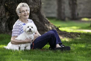 Senior woman sitting in the grass with a small white dog