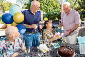 Four senior men and a senior woman celebrating a birthday on a patio at Westminster Gardens