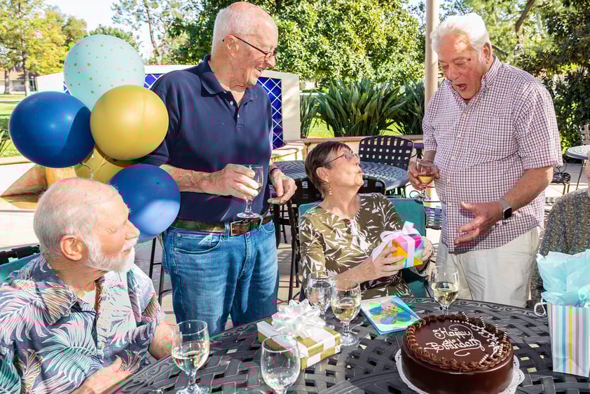 Four senior men and a senior woman celebrating a birthday on a patio at Westminster Gardens
