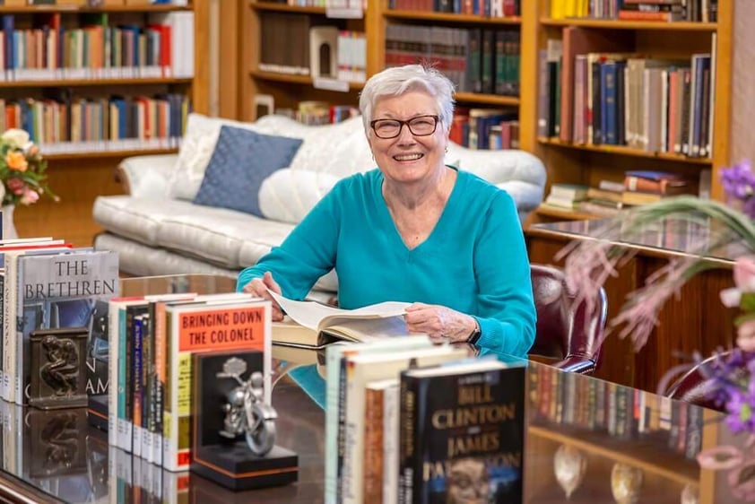 Senior woman with a book at a table in the library at Westminster Gardens