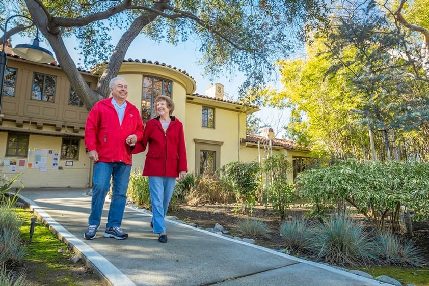 Senior couple wearing red jackets walking away from the Morrison House at Westminster Gardens