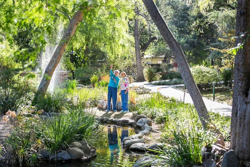 Two senior women — one pointing up — next to the pond at Westminster Gardens