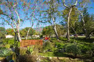 Senior couple wearing red jackets walking toward a bridge on the landscaped grounds of Westminster Gardens