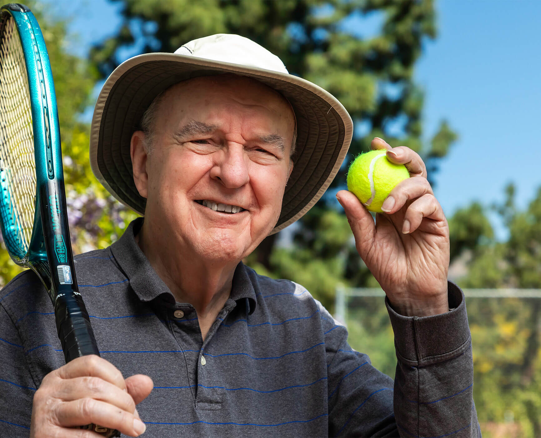 Close-up of a senior man wearing a bucket hat and holding a tennis racket
