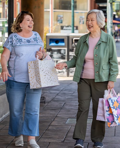 Two senior women holding shopping bags and walking through town