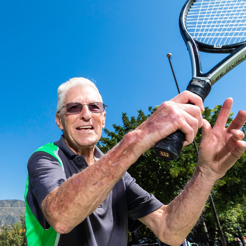 Senior man smiling holding up a tennis racket