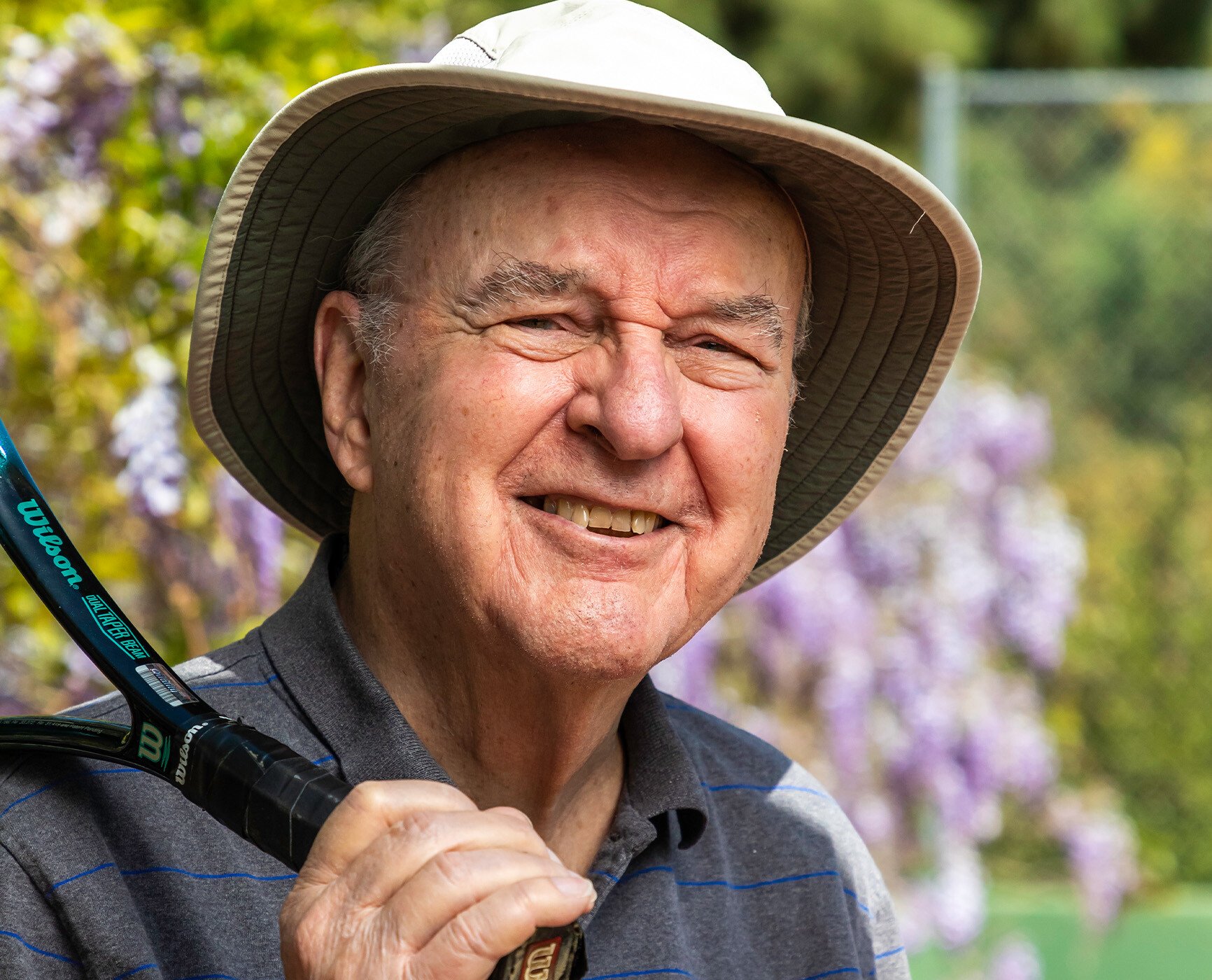 Close-up of a senior man wearing a bucket hat and holding a tennis racket