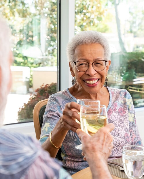 Two seniors toasting with glasses of white wine in the Westminster Gardens dining room