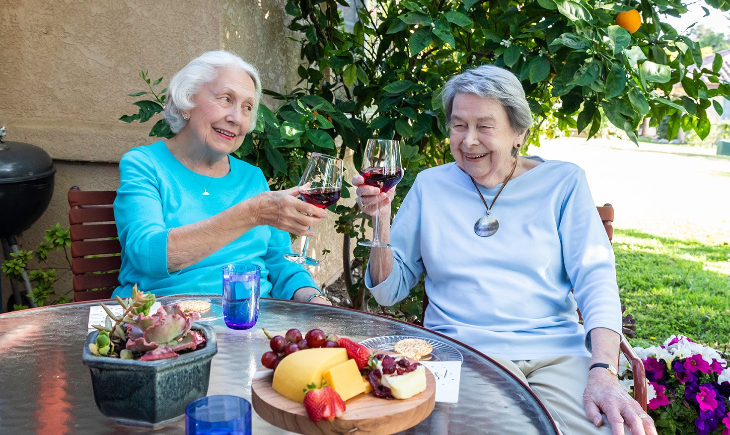Two senior women with glasses of red wine sitting on the patio of a Westminster Gardens home