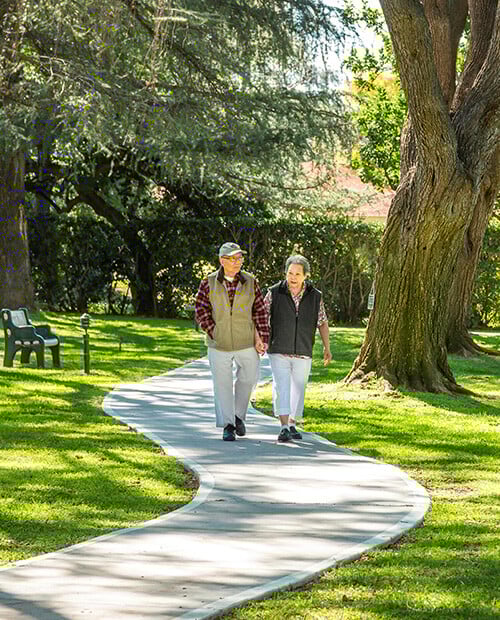 Senior couple walking on a paved path through the landscaped grounds of Westminster Gardens