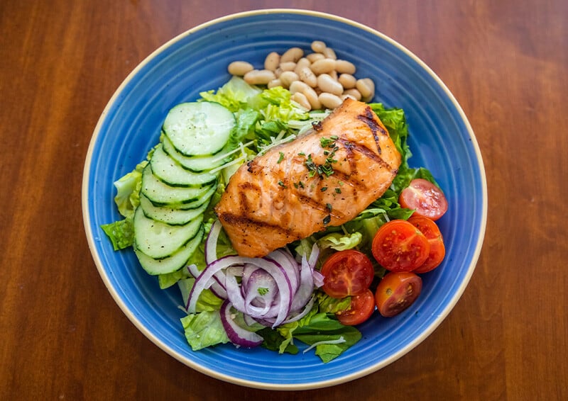 Salmon filet on a bed of lettuce, cucumber, onion, tomato and beans