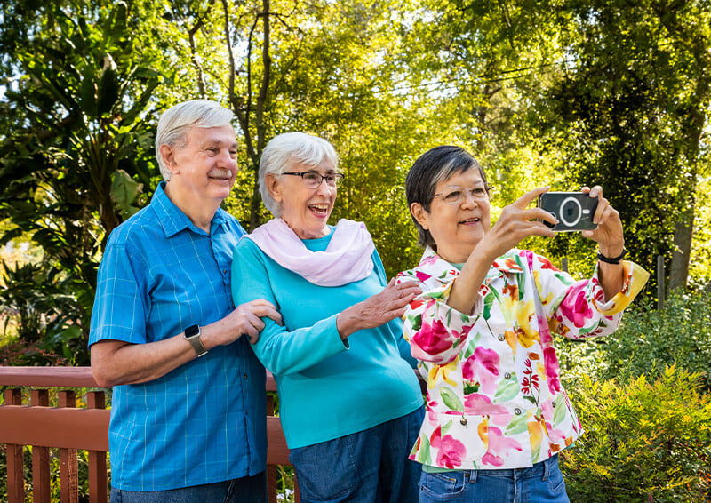 Two senior women and a senior man taking a selfie on the grounds of Westminster Gardens