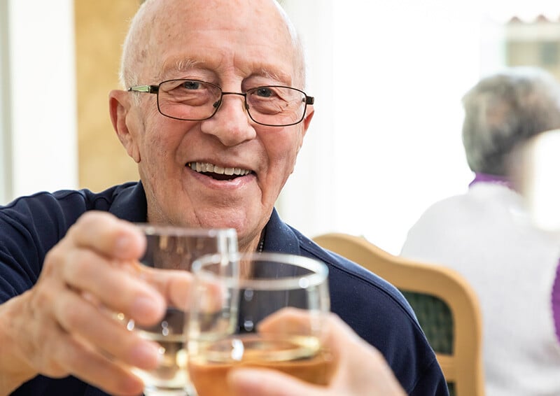 Senior man toasting with a glass of wine in the dining room at Westminster Gardens