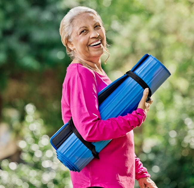 Women smiling to the camera holding a yoga mat