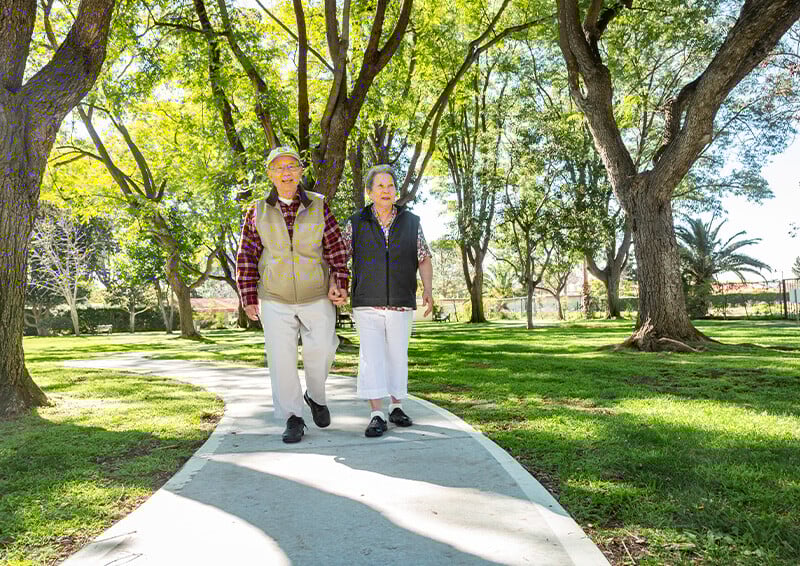 Senior couple holding hands and walking on a paved path through the grounds of Westminster Gardens