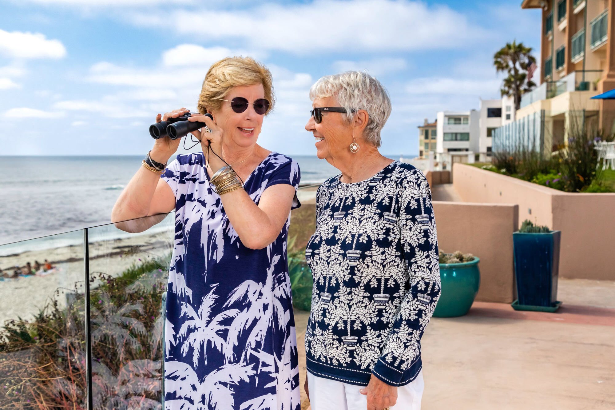 Two women with binoculars on a terrace overlooking the ocean.