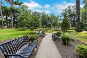 Paved walkway with benches in a lush park setting, outside The Mansion at Rosemont