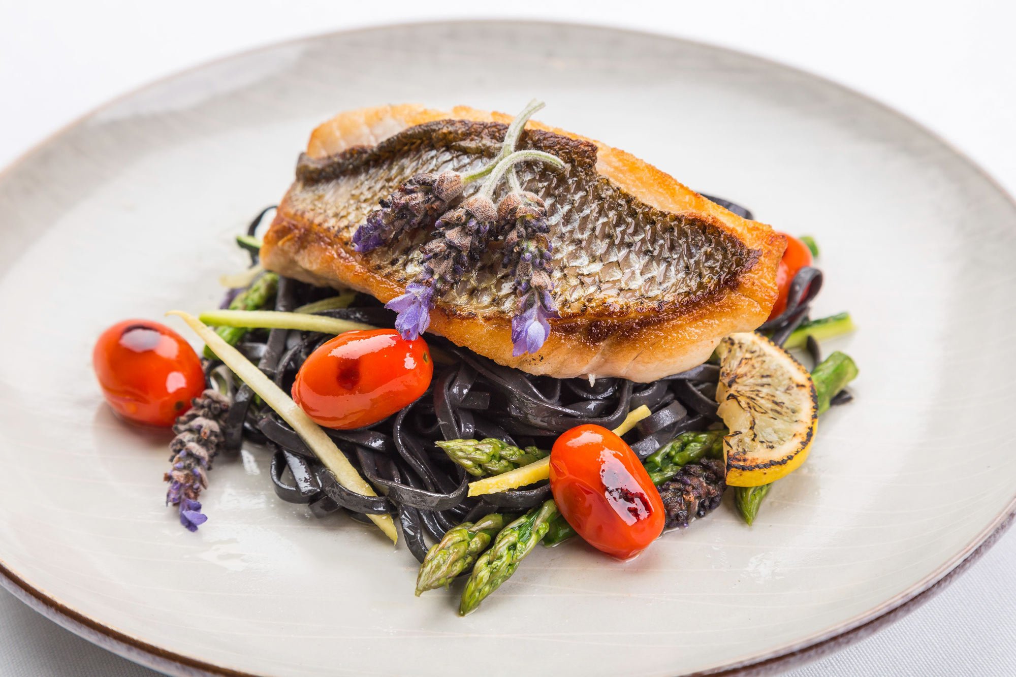 Grilled fish served over black pasta with tomatoes, asparagus, and lemon.