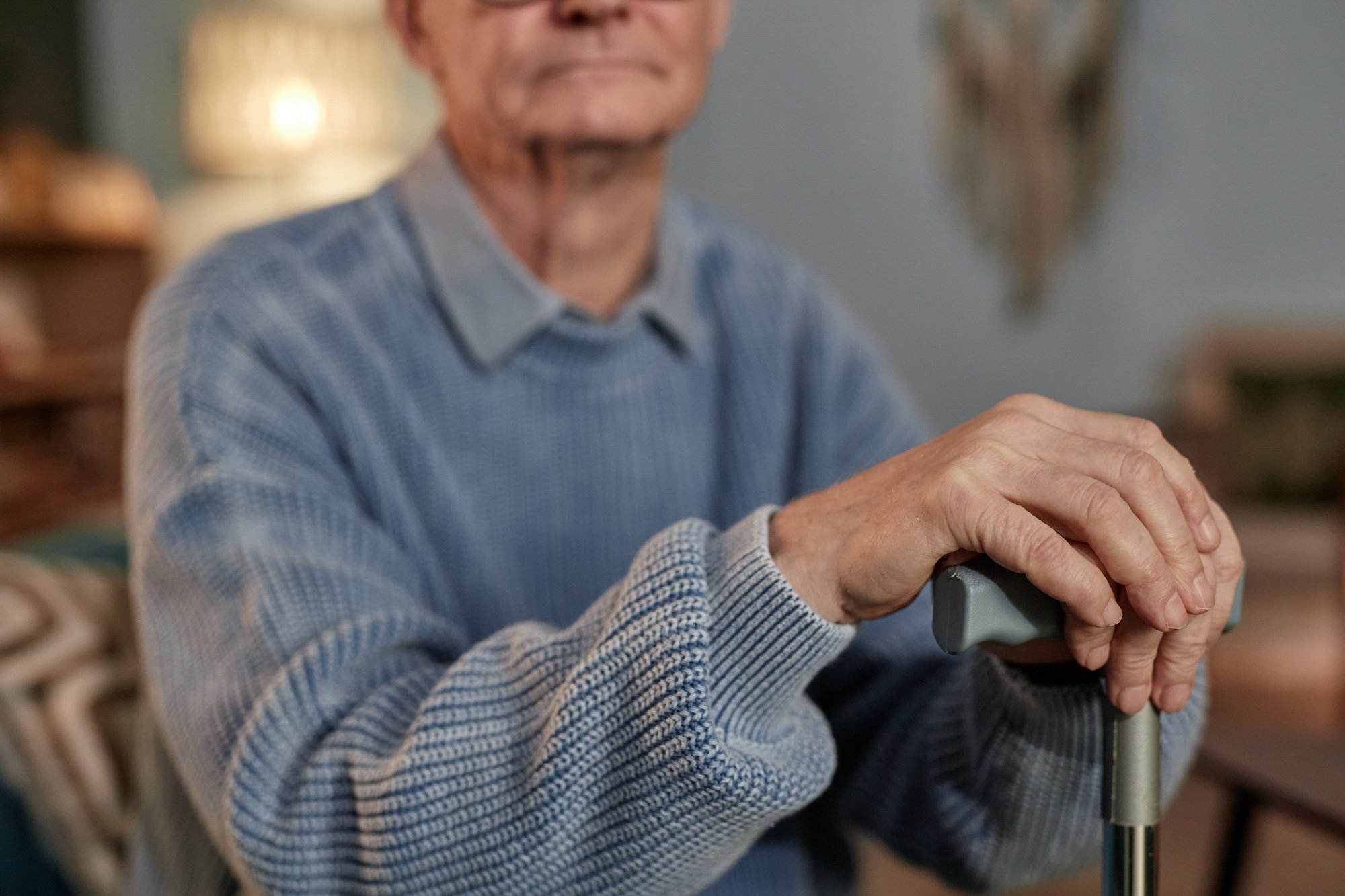 elderly man in a blue sweater leaning on his cane while he sits on the couch