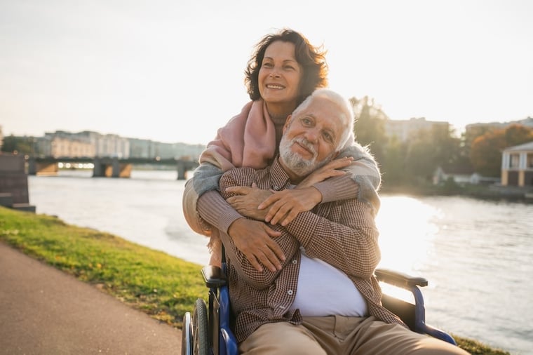 A couple spending time together outside. One person is caregiving for her spouse, who uses a wheelchair.