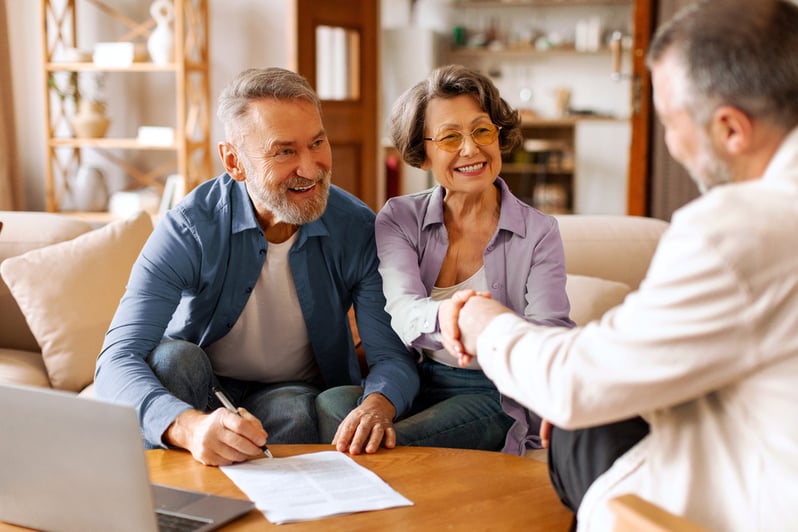 A couple smiling as they shake hands with a man across from them.