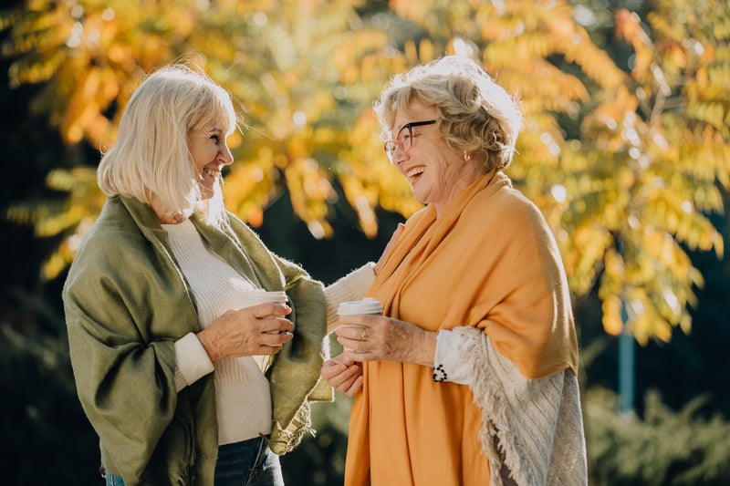 two women smiling outside and drinking coffee