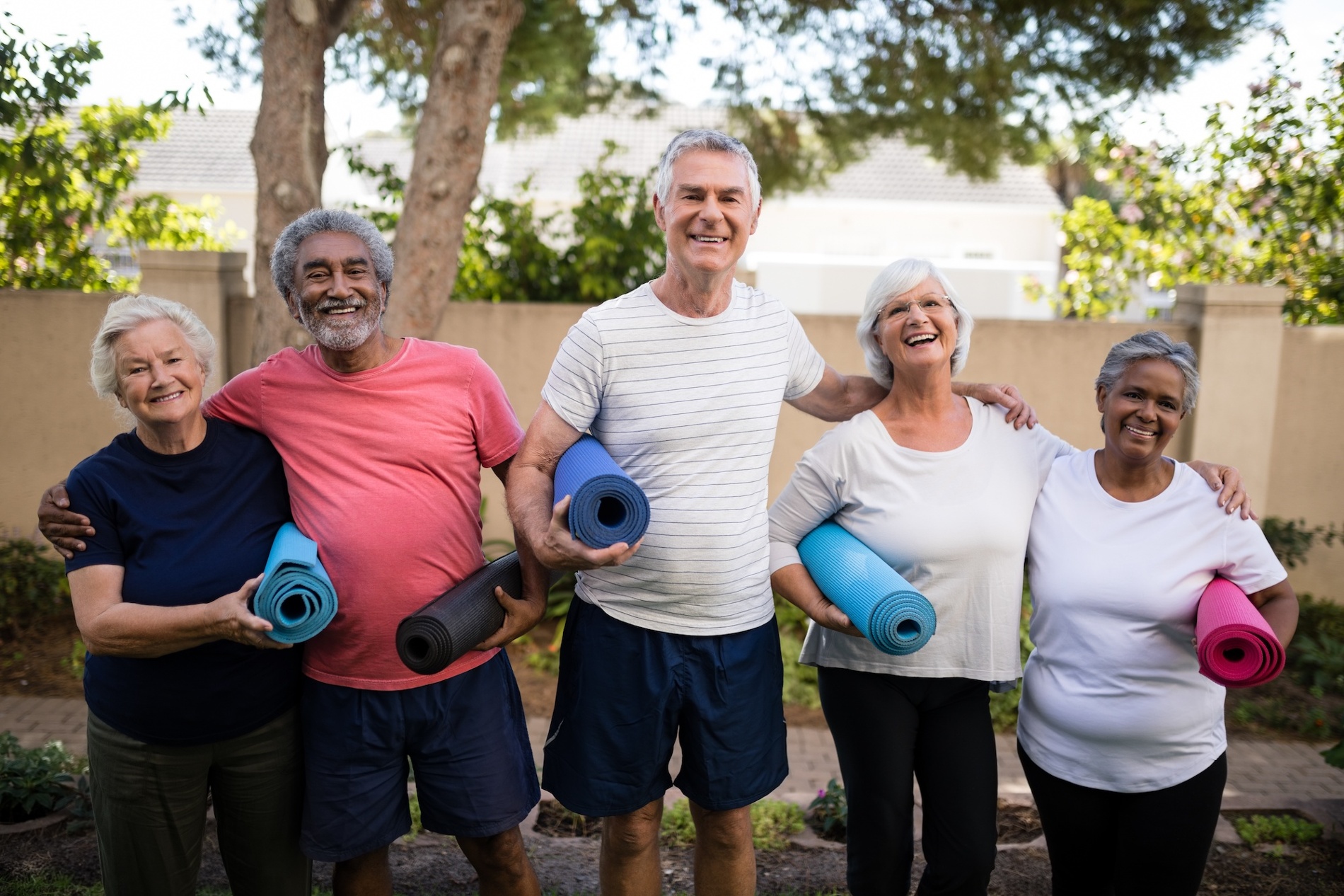 A group of 5 healthy seniors smiling at the camera and holding yoga mats