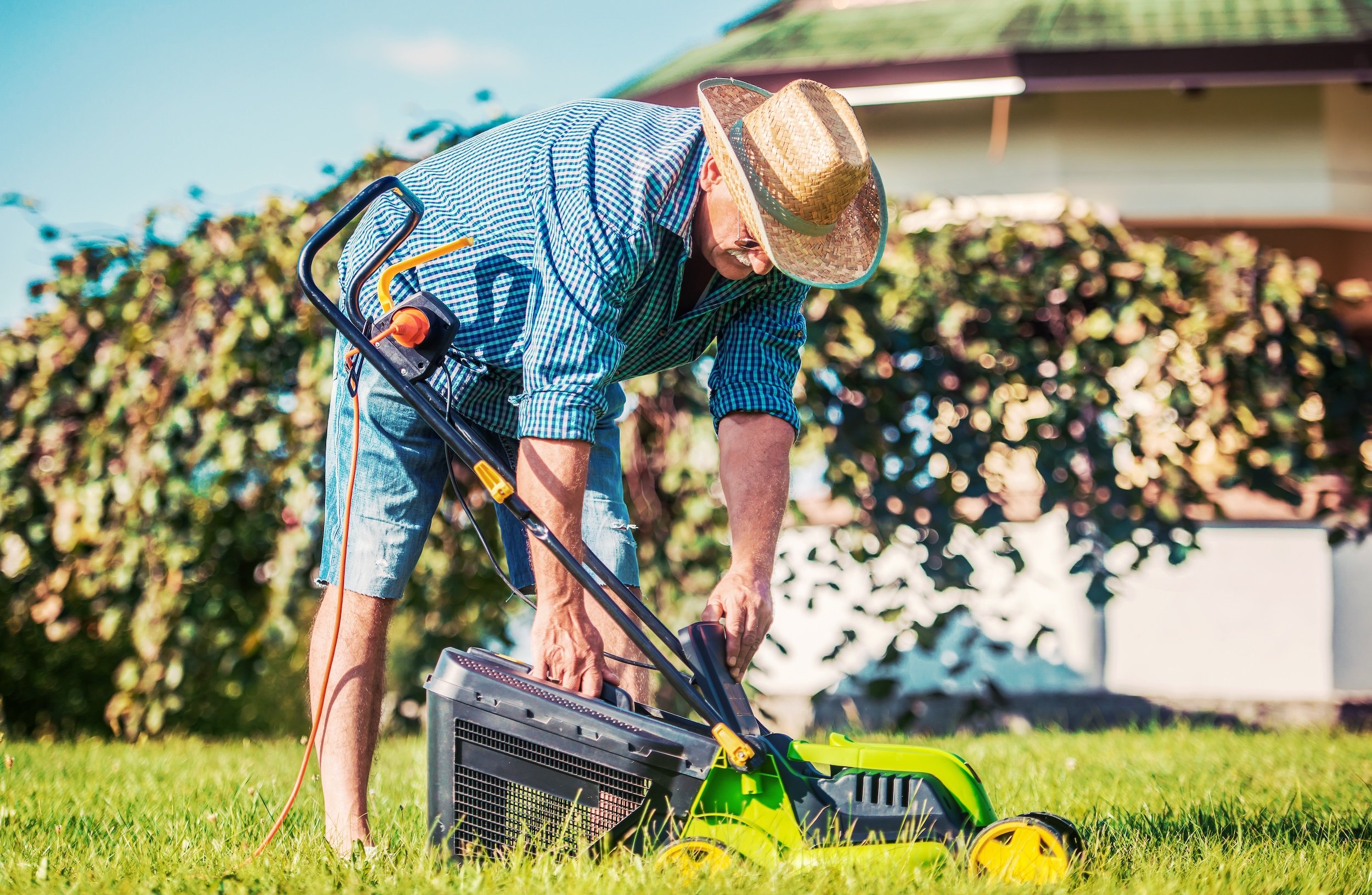 older man bending down to fix his lawnmower outside