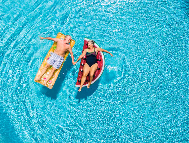 senior couple lounging on pool floats holding hands and looking at each other