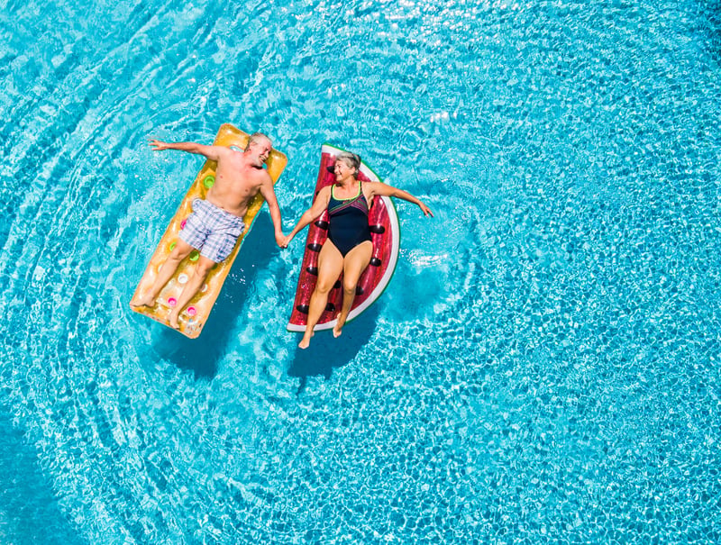 senior couple lounging on pool floats holding hands and looking at each other