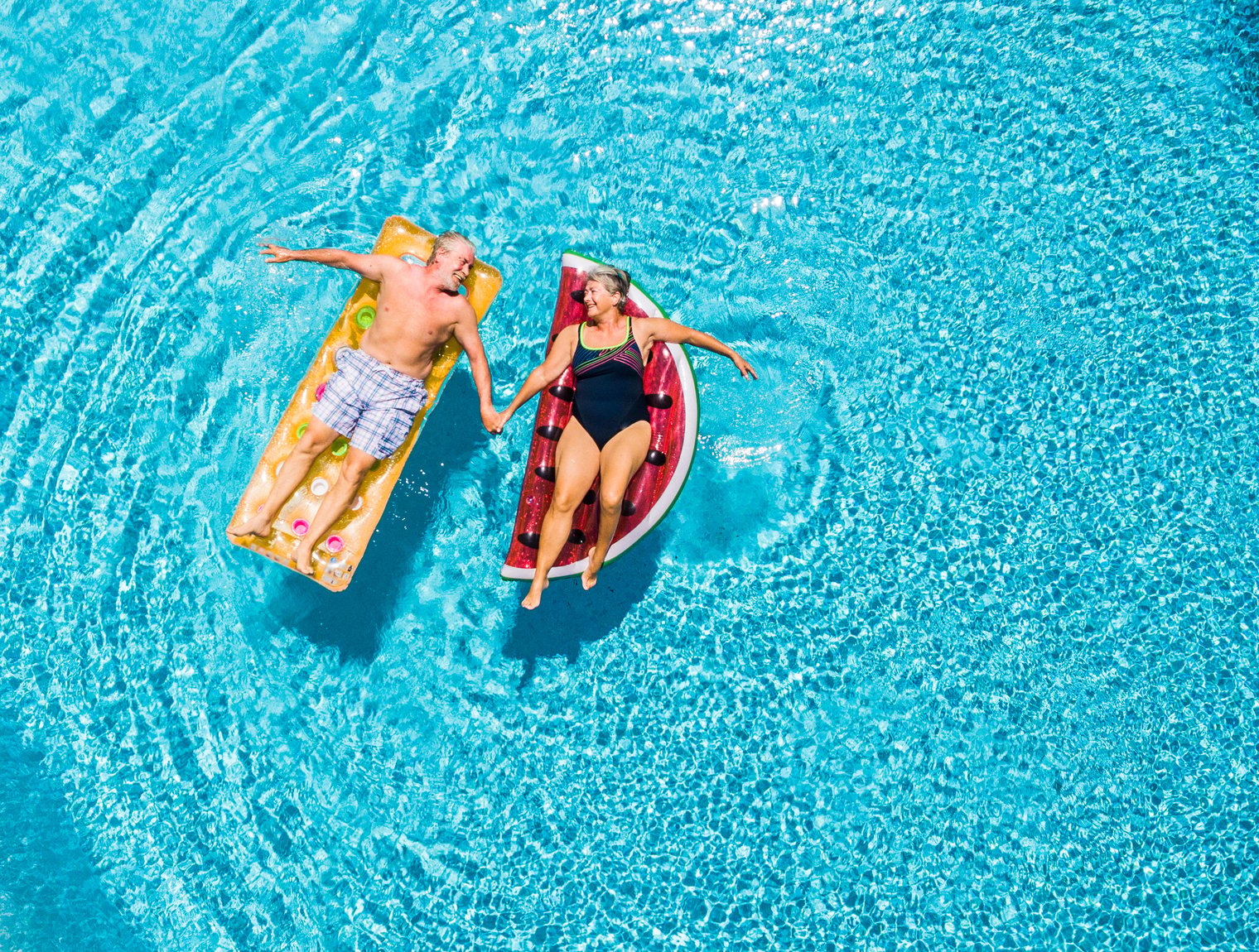 senior couple lounging on pool floats holding hands and looking at each other