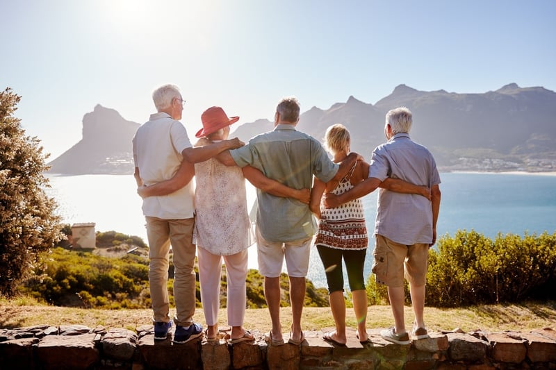 group of senior friends standing on a rock ledge and admiring the mountain views while wrapping their arms around each other