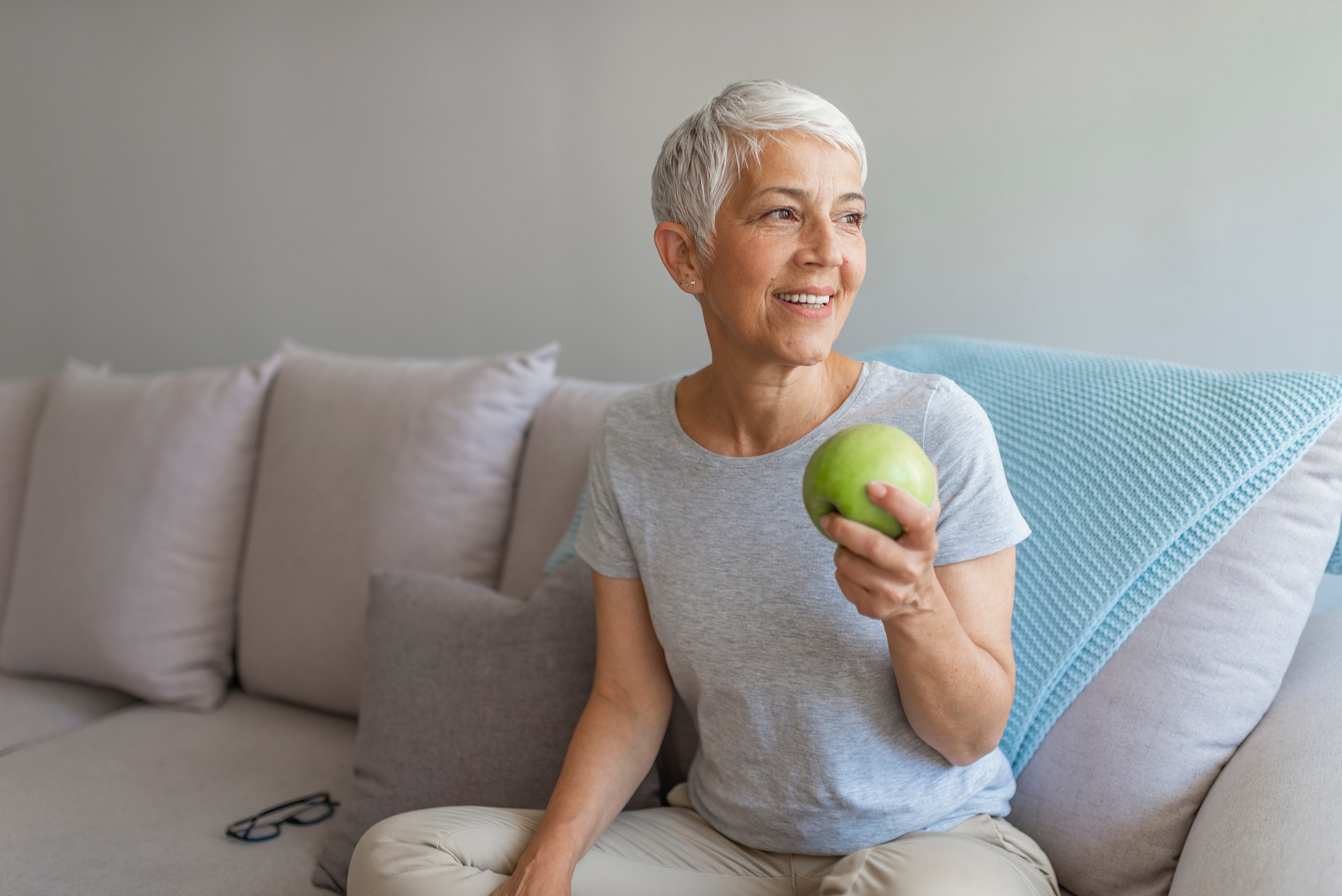 Woman sitting on couch smiling and eating an apple