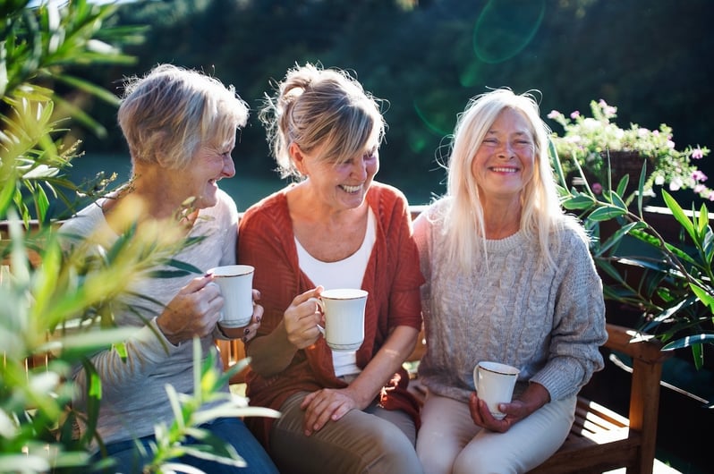 three women sitting on a bench drinking coffee outside