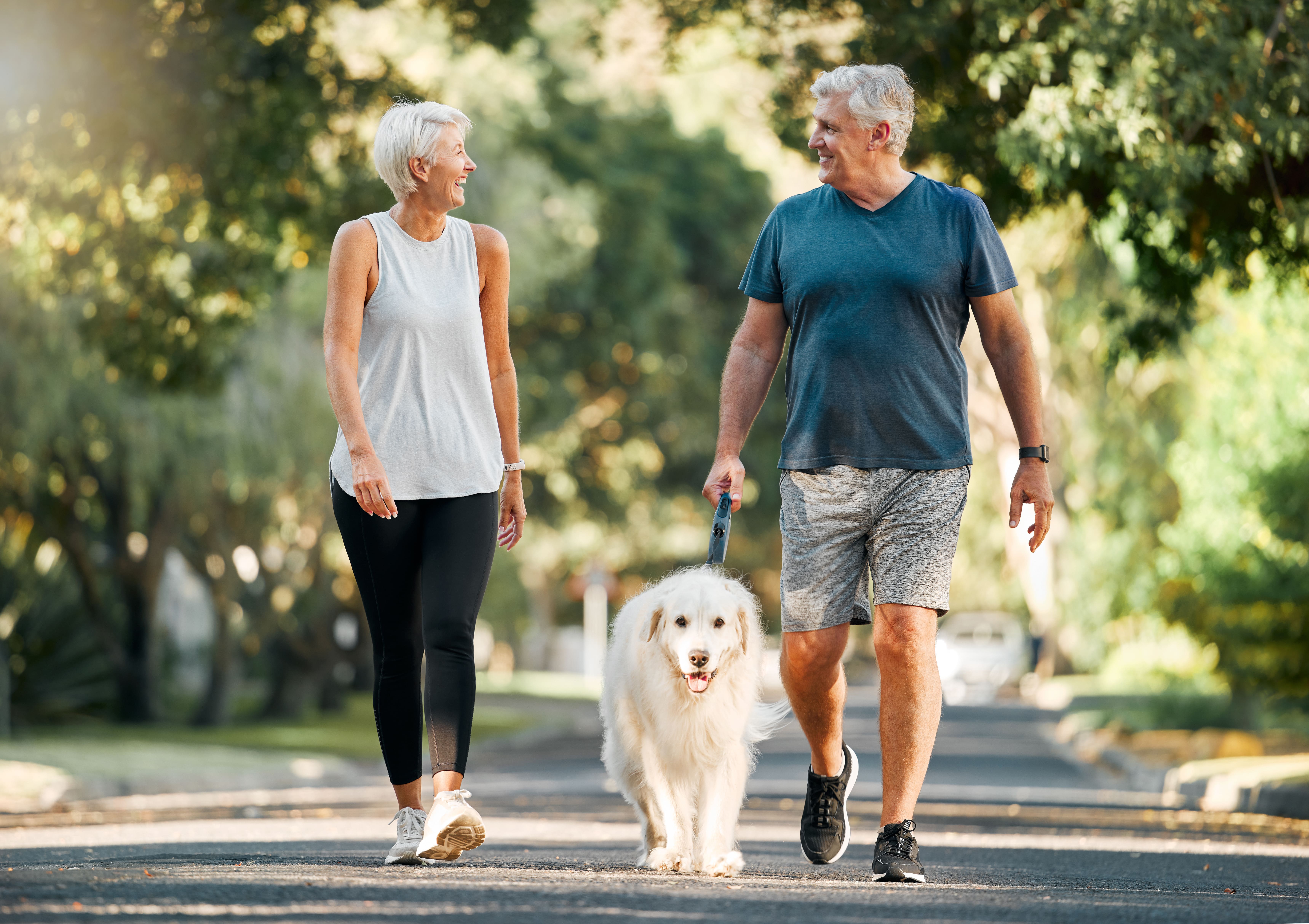 man and woman smiling and walking dog outside