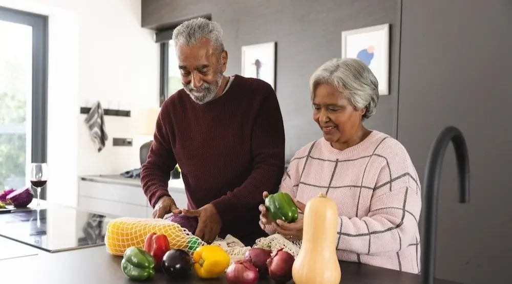 A couple smiles while preparing vegetables in a modern kitchen.