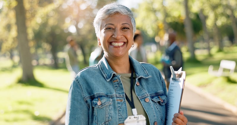 senior woman holding a clipboard and smiling outside in park