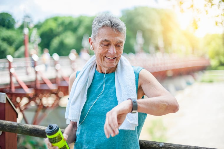 A resident with a towel draped over their shoulders holding a water bottle, checks their watch for fitness information. 