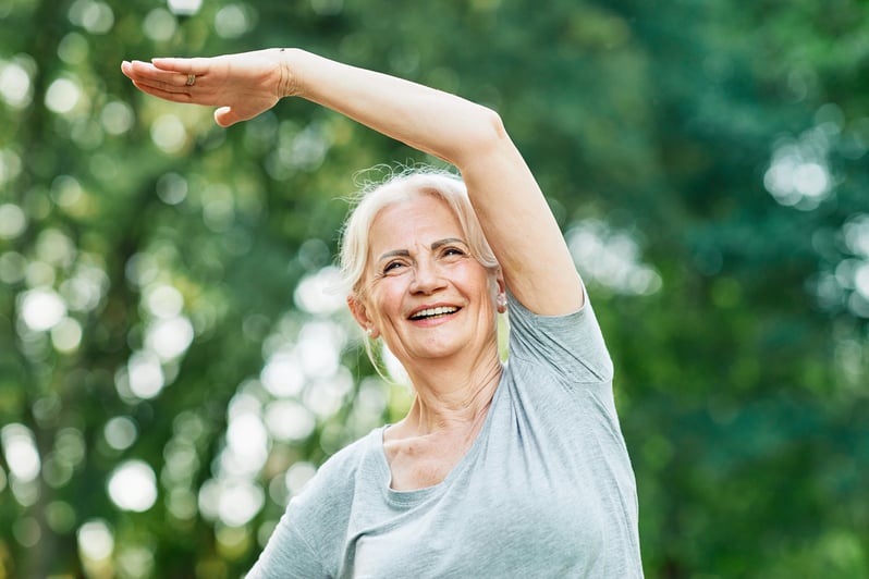 Woman smiling with arm raised against a blurred green background.